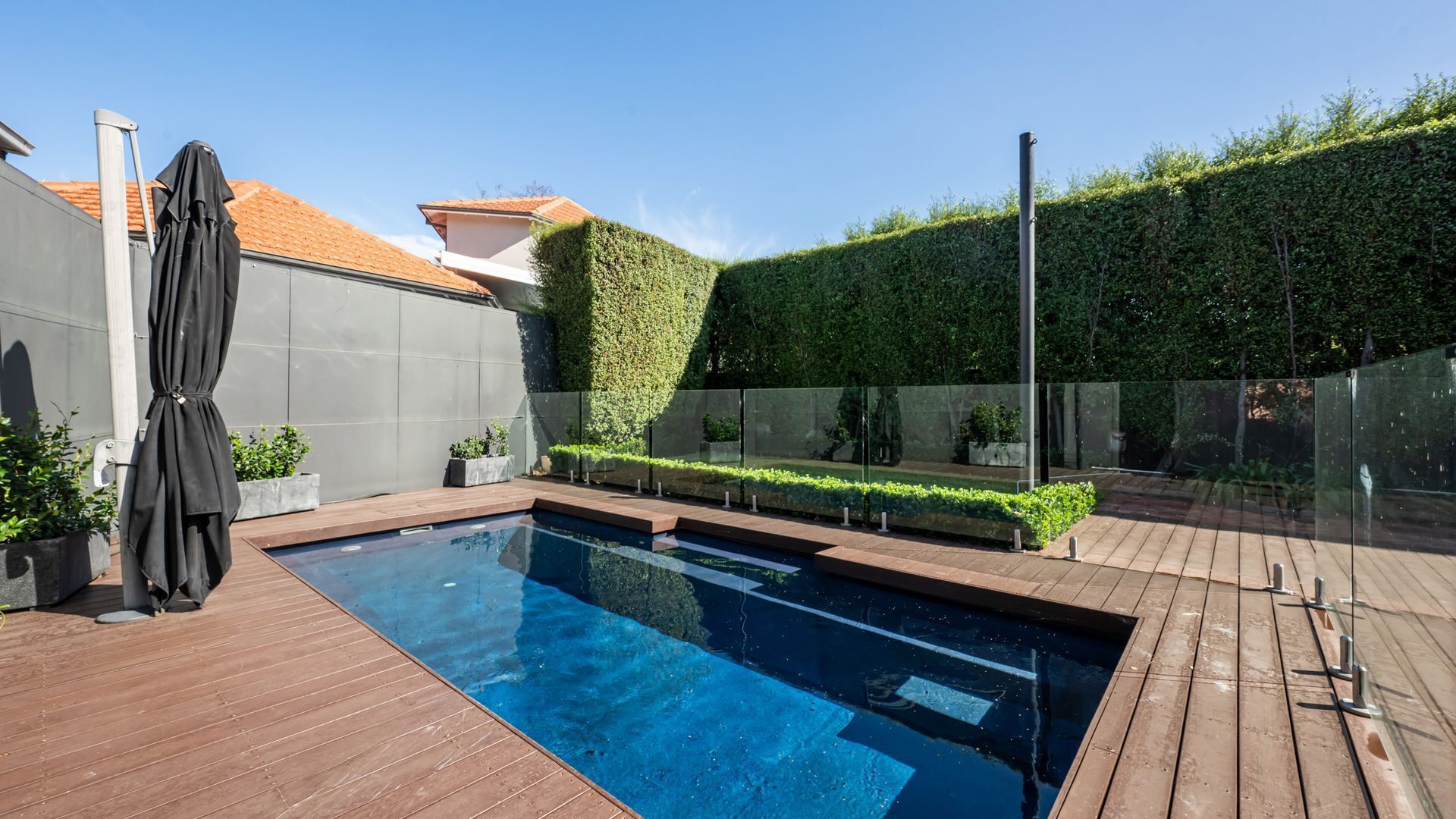 Una piscina amb una terrassa de fusta, una tanca i una tanca de vidre.