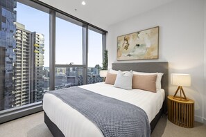 Ein modernes Schlafzimmer mit einem großen Bett, Blick auf die Stadt, einem Bild an der Wand und einer Nachttischlampe.