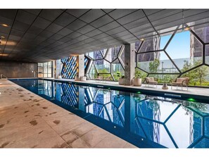 Ein moderner, überdachter Pool mit geometrischen Glaswänden, Sitzbereichen und freiem Blick auf die Stadt.