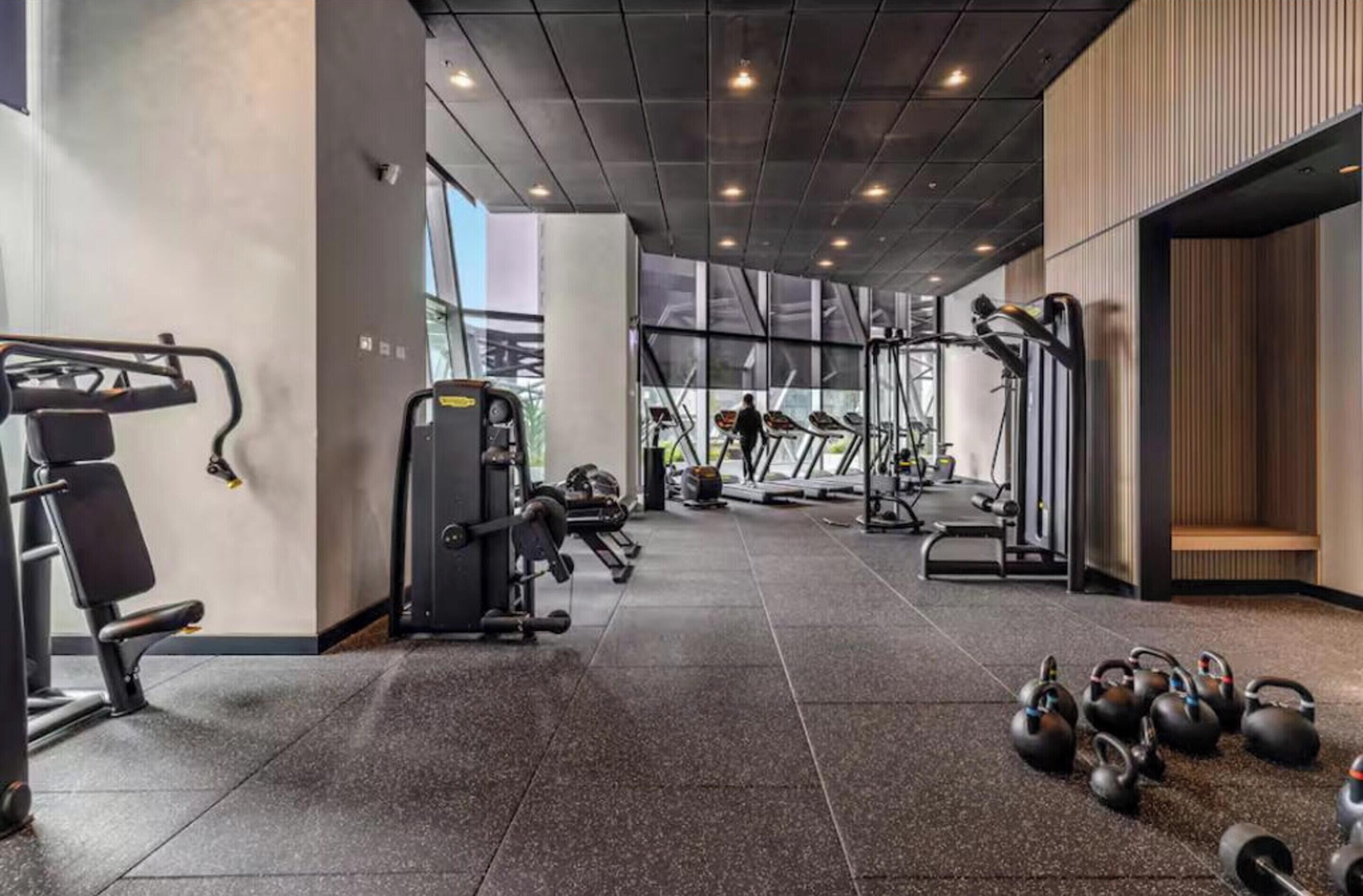 Une salle de sport équipée de divers appareils d’exercice, d’un tapis de course et de kettlebells.