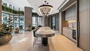 A modern kitchen with a marble island, pendant lighting, and a view of the city. - Skyline & Sea Luxe Heated Pool, Gym, Sauna, Steam (Melbourne)
