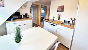 Een kleine keuken met een magnetron, koffiezetapparaat en een spoelbak. Er staat een eettafel met stoelen en een potplant.