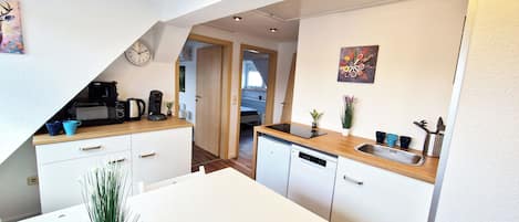 A compact kitchen with a microwave, coffee maker, and a sink. There is a dining table with chairs and a potted plant.
