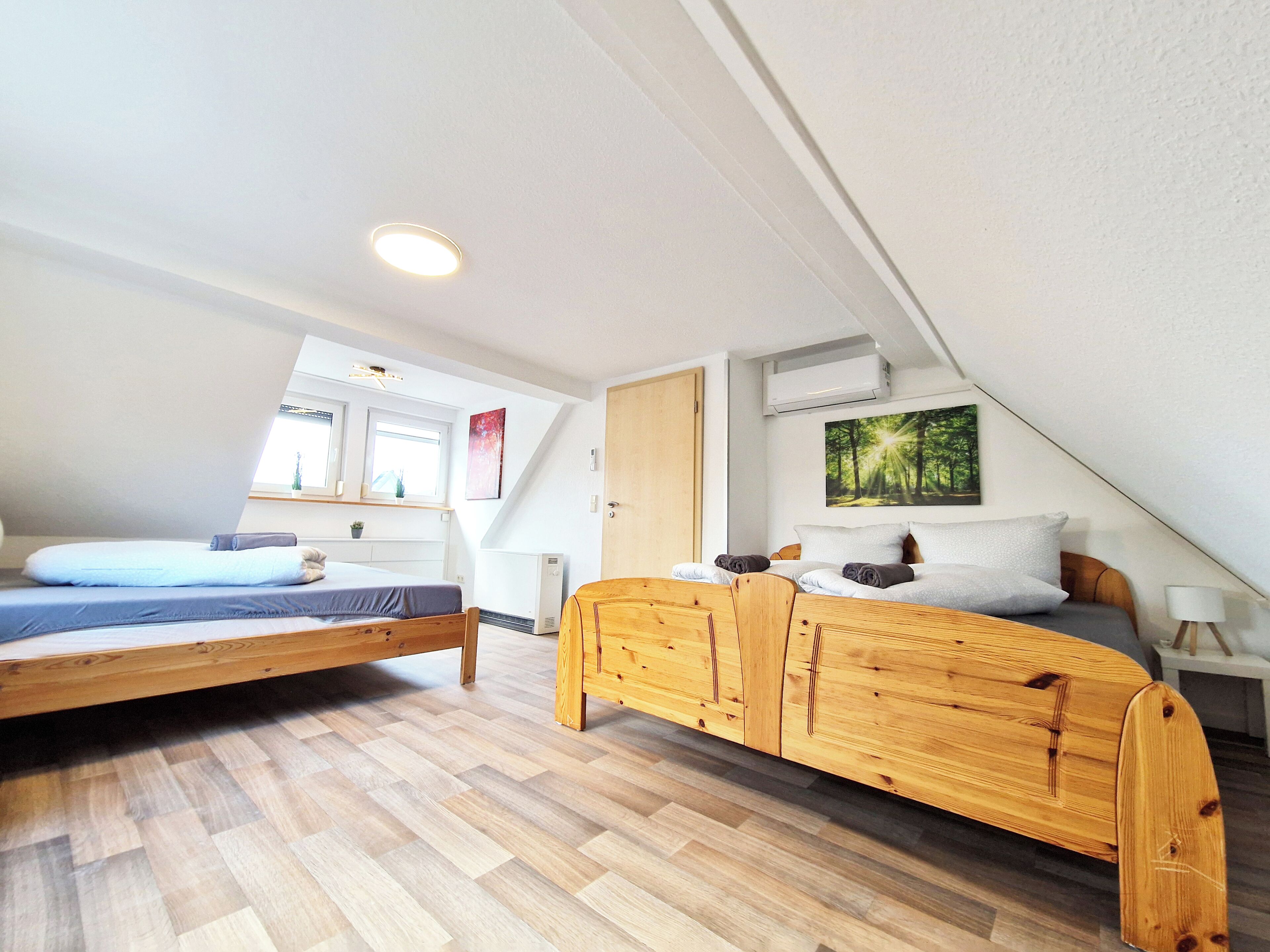 A bedroom with two beds, a wooden wardrobe, a window, and a wall-mounted air conditioner.