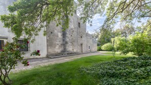 Un edificio histórico de piedra con un patio empedrado, rodeado de abundante vegetación y árboles.