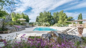 Un área de piscina con pared de piedra, sillones de descanso y una pérgola.