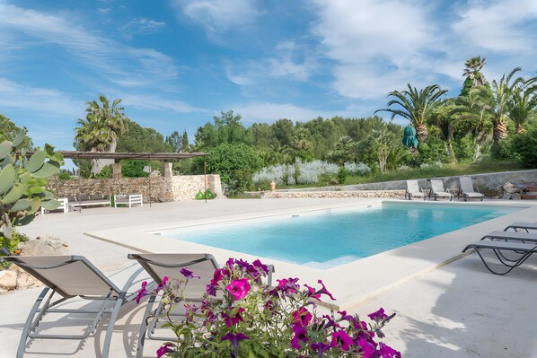Ein Poolbereich mit Liegestühlen, einer Pergola und einer Steinmauer.