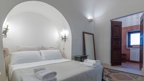 Habitación de hotel con una cama grande, un espejo, una mesita de noche y vistas de la habitación contigua.