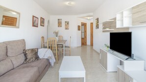 A modern living room with a sofa, a coffee table, a TV, and a dining area with chairs and a table. - Casa Andrés – Families Only, with Balcony, Wi-Fi, and Air Conditioning (Conil de la Frontera)