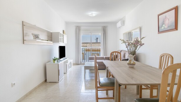 A dining area with a wooden table, chairs, a vase with flowers, and a television on a stand. - Casa Andrés – Families Only, with Balcony, Wi-Fi, and Air Conditioning (Conil de la Frontera)