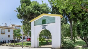 A white archway with green and yellow accents, labeled 'URBANIZACION LOSORE DE LA VILLA,' leading to a park area with trees and a building in the background. - Casa Andrés – Families Only, with Balcony, Wi-Fi, and Air Conditioning (Conil de la Frontera)