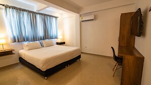 Un dormitorio con cama, mesitas de noche, escritorio y aire acondicionado.