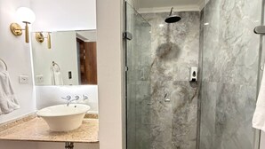 Un baño con ducha de vidrio, lavamanos con espejo y perchero para toallas.