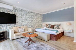 Une chambre d’hôtel moderne équipée d’une télévision à écran plat, d’un canapé, d’un lit avec une tête de lit en bois et d’une petite table d’appoint.