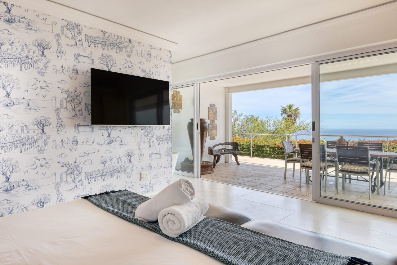 A hotel room with a bed, a flat-screen TV, a balcony with a table and chairs, and a view of the sea.