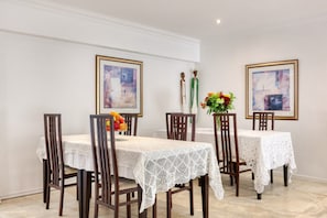 A dining area with a table set for four, featuring a white lace tablecloth, wooden chairs, and framed artwork on the walls. - Entabeni Guest House - over 20 years of Camps Bay experience (Cape Town)