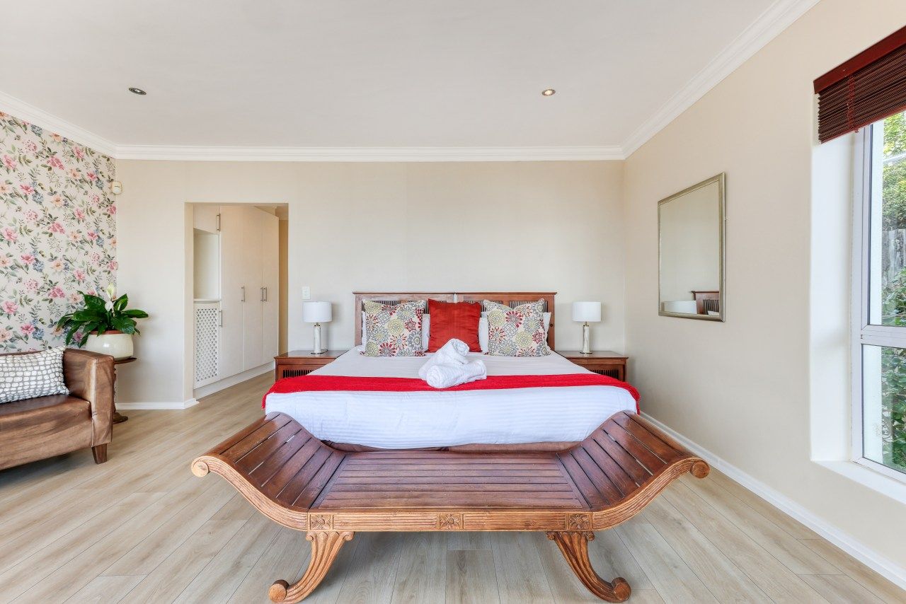 A bedroom with a large bed, a wooden bench, a nightstand, a mirror, and a window.