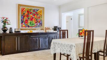 A dining area with a table set for four, a kitchen counter with various appliances, and a large painting on the wall.