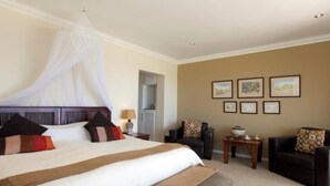 Een slaapkamer met een hemelbed, een bank, een klein tafeltje en ingelijste foto's aan de muur.