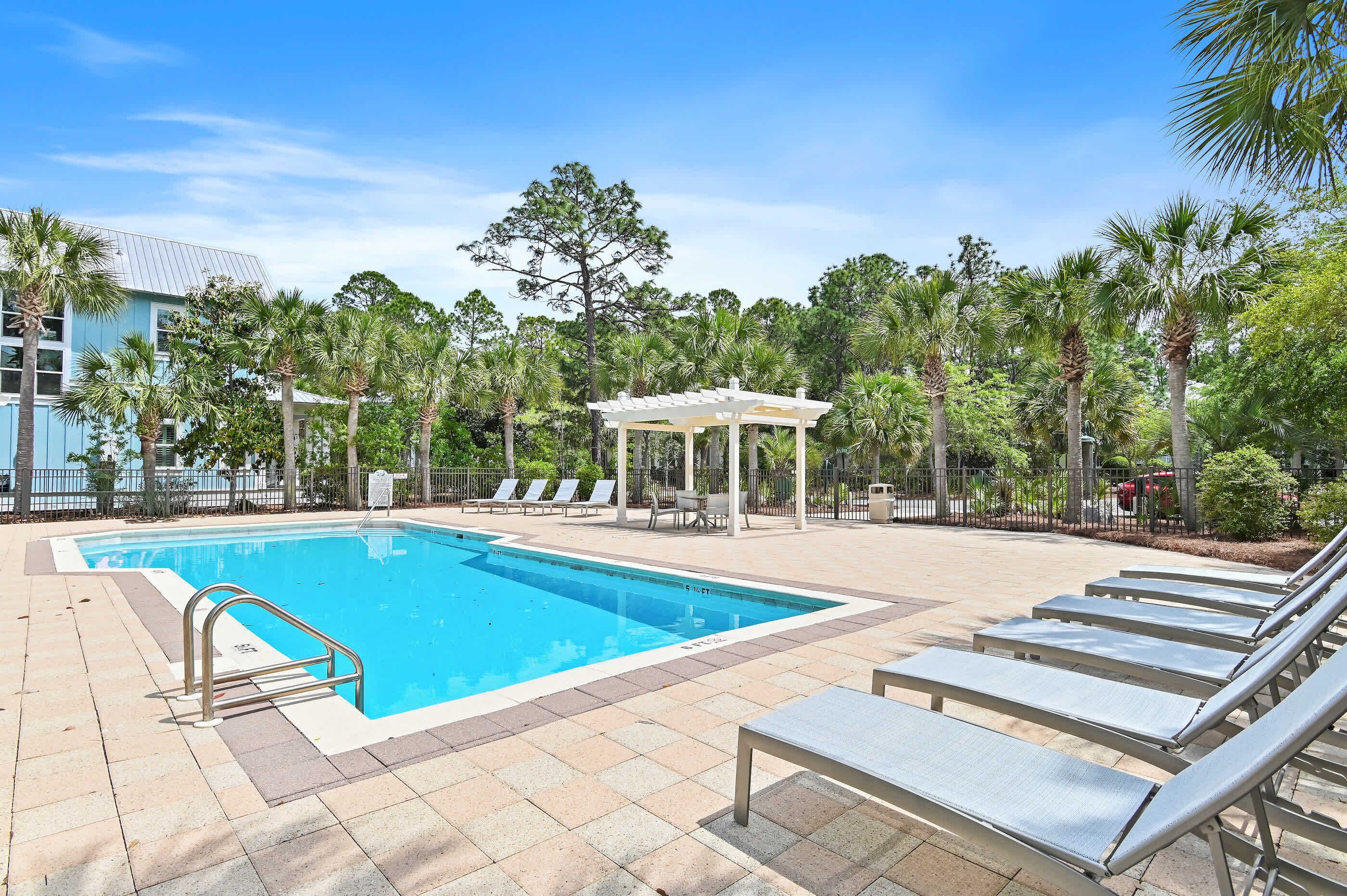 A swimming pool with lounge chairs, a gazebo, and palm trees.