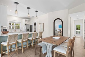 A modern kitchen with a wooden dining table, chairs, and pendant lights. - Avia Laura | 6-Seater Golf Cart | Fenced-In Yard (Santa Rosa Beach)