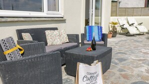 Et udendørs opholdsområde i flet, med puder, en flaske vin og en taske fra Cornish Cottage Holidays.