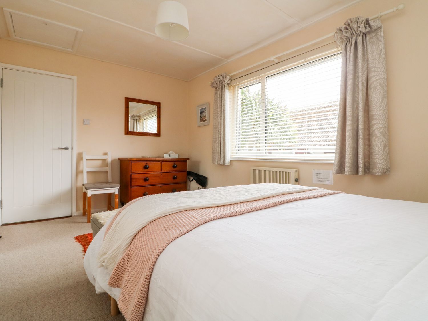 A bedroom with a bed, a dresser, a chair, a window with curtains, and a radiator.