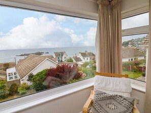 Una habitación con un ventanal amplio que da a un pueblo costero, una cama con almohadillas estampadas y vistas al mar.