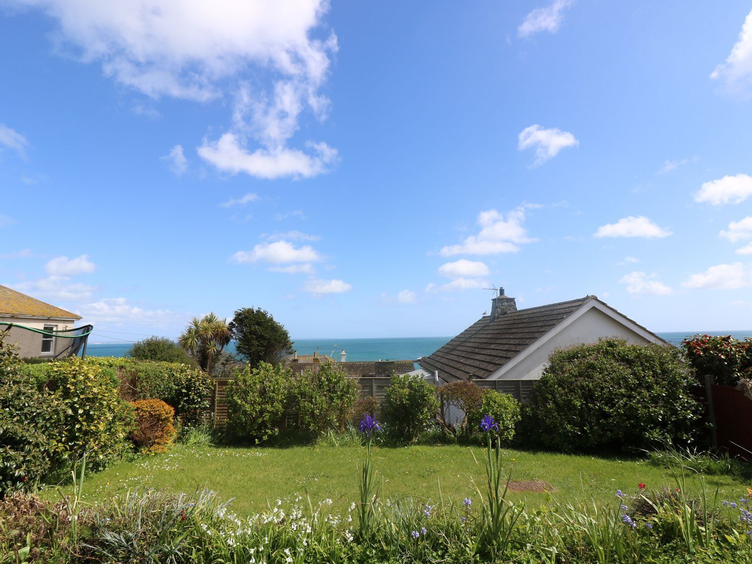 Een huis aan de kust met een tuin, uitzicht op zee en een heldere lucht.