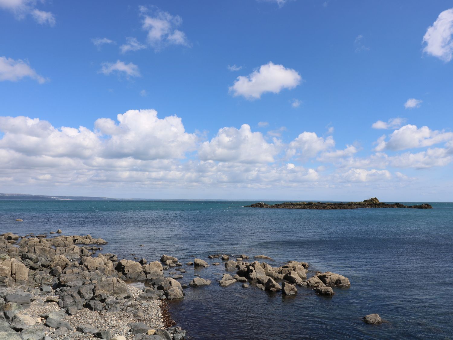 Costa rochosa com águas calmas e uma ilha ao longe.