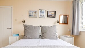 A bed with two pillows, a bedside table with a lamp, and three framed pictures on the wall. - Wootton Gray (Penzance)