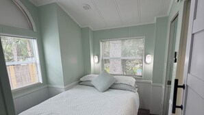 Een slaapkamer met een bed, twee ramen met zonwering, een plafondventilator en een deur.