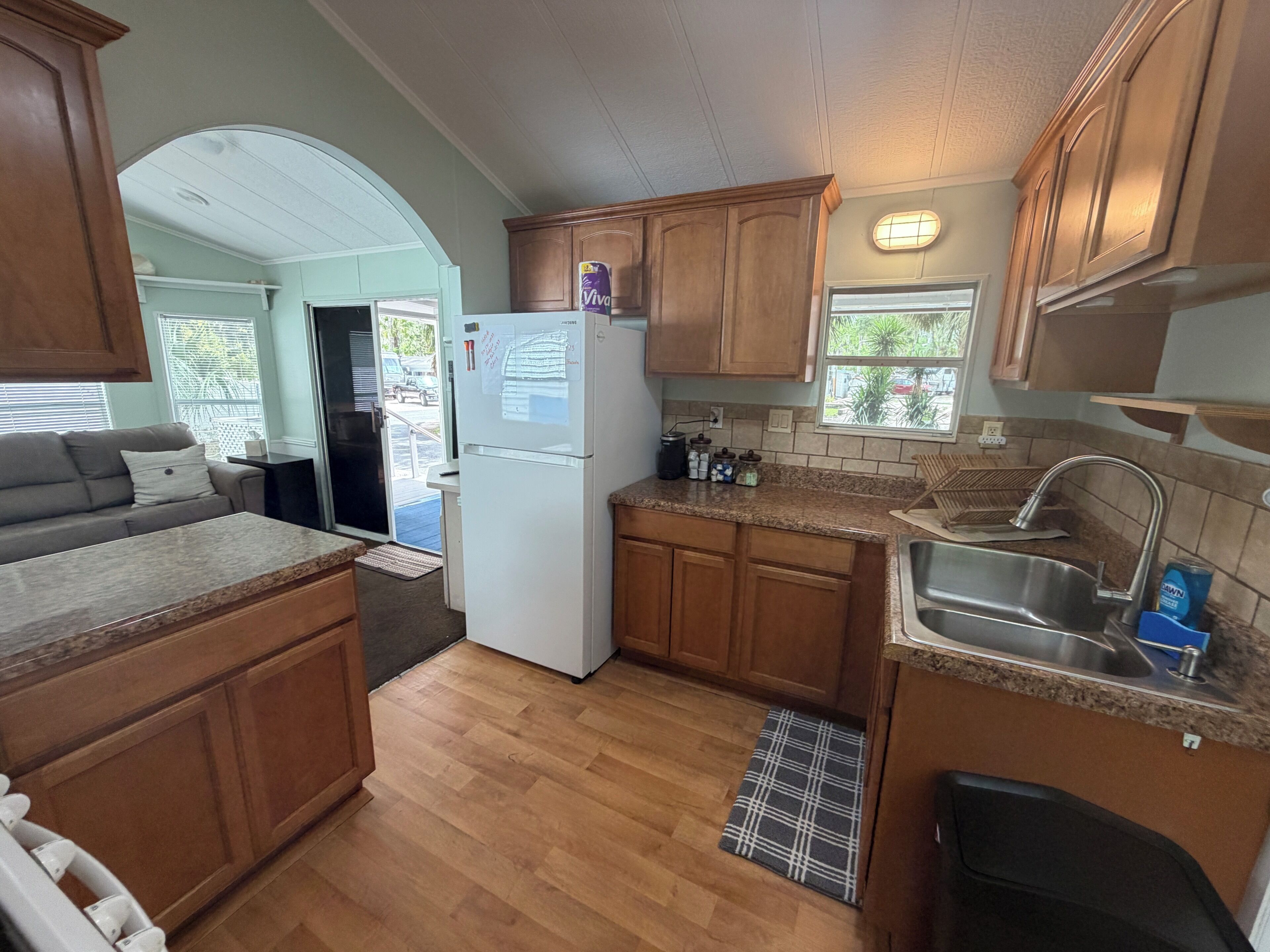 A compact kitchen with wooden cabinets, a refrigerator, a sink, and a window overlooking a parking area.
