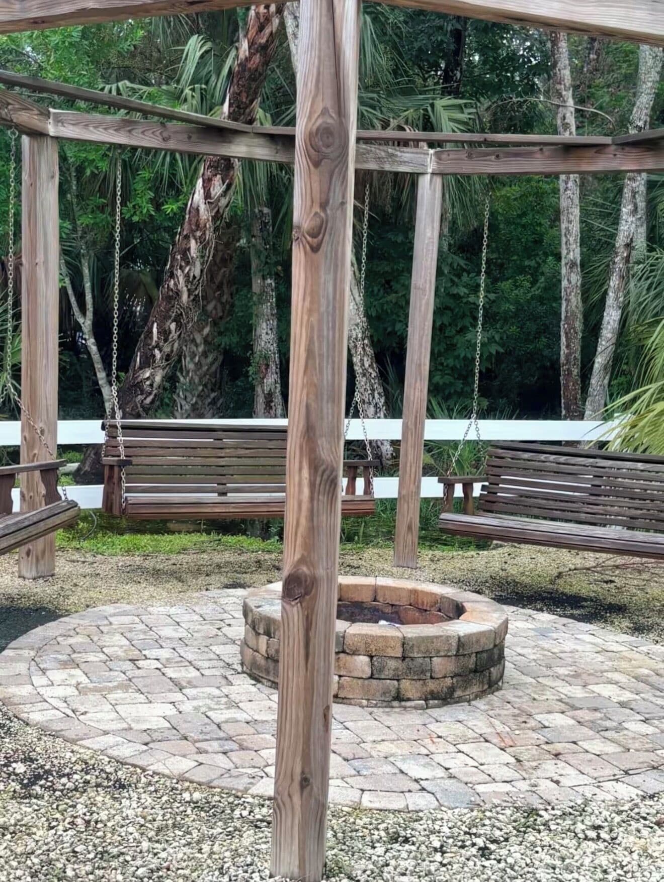 A wooden swing set, a stone fire pit, and a bench in a park setting.