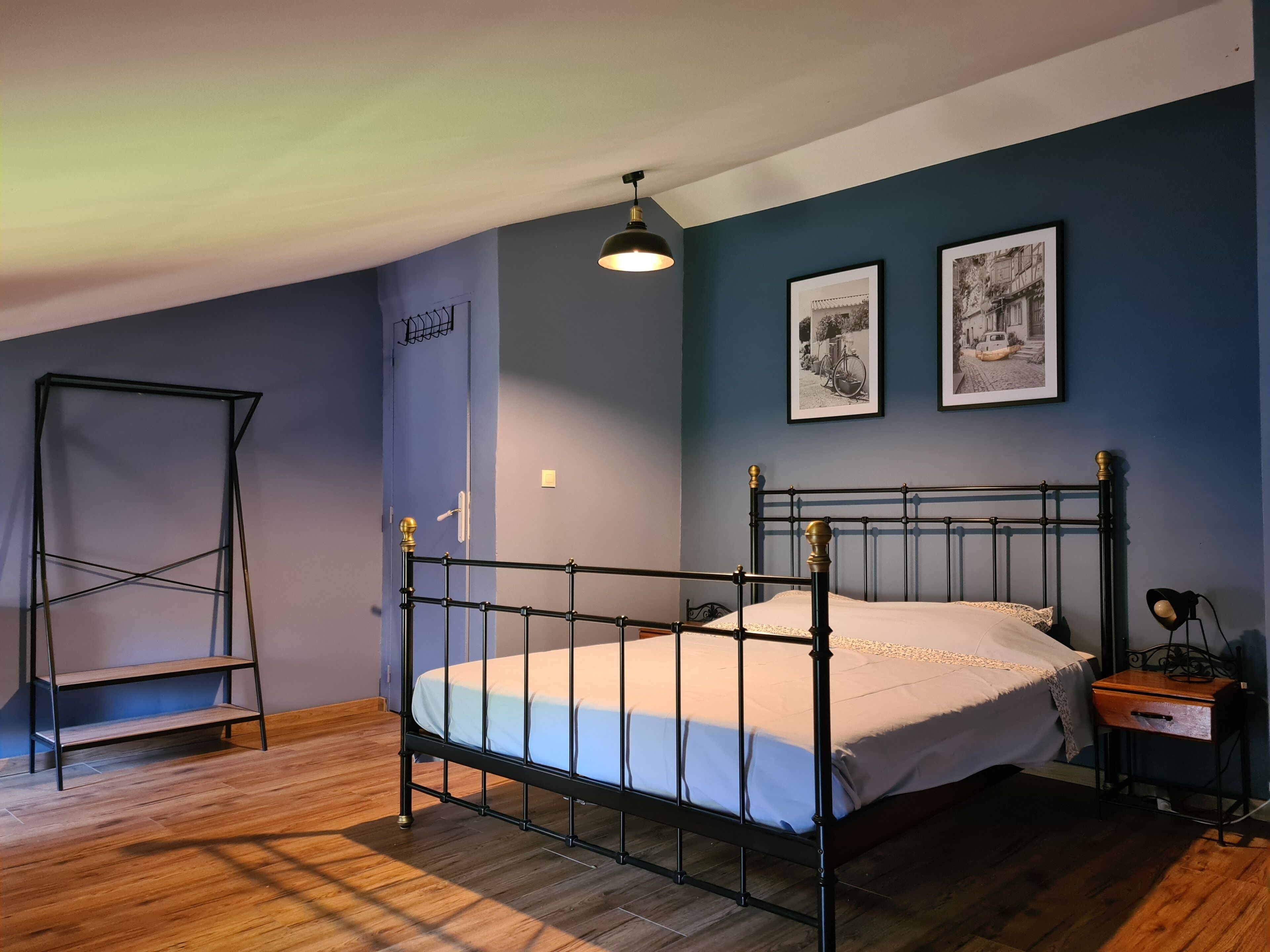 Ein Schlafzimmer mit einem Metallbettgestell, Holzboden, einem stehenden Regal und zwei gerahmten Bildern an der Wand.