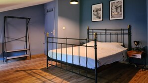 Quarto com estrutura de cama em metal, piso de madeira, estante e duas imagens emolduradas na parede.