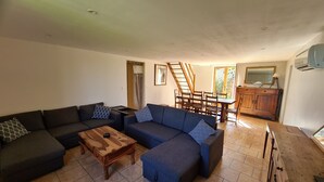 Uma sala de estar com sofá seccional, mesa de centro de madeira, área de jantar com mesa e cadeiras de madeira, e cozinha com armário de madeira e espelho.