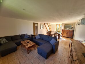 A living room with a sectional sofa, a wooden coffee table, a dining area with a wooden table and chairs, and a kitchen area with a wooden cabinet and a mirror. - Spacious 5 bedroom family home in the picturesque medieval village of Belvès (Pays de Belvès)