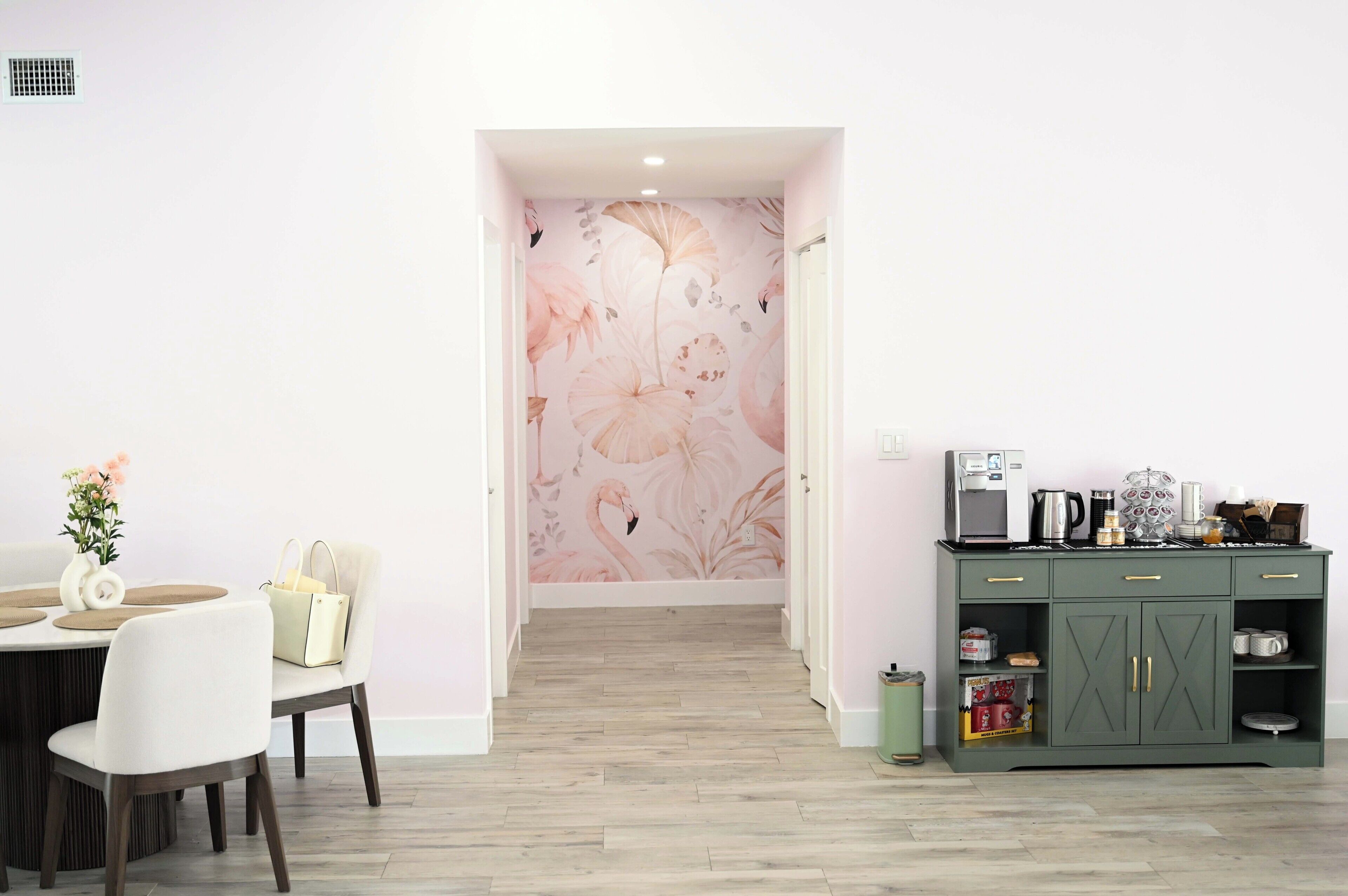 Ein Zimmer mit Esstisch, Stühlen, einem grünen Schrank mit Küchengeräten und floralem Wandpapier.