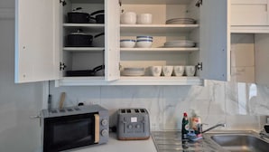 A kitchen with a microwave, toaster, and open cabinet with dishes and cookware. - Private room in Little Bridgeford (Stafford)