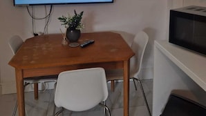 A room with a TV displaying 'WELCOME,' a dining table with chairs, a potted plant, and a microwave on a shelf. - Private room in Little Bridgeford (Stafford)