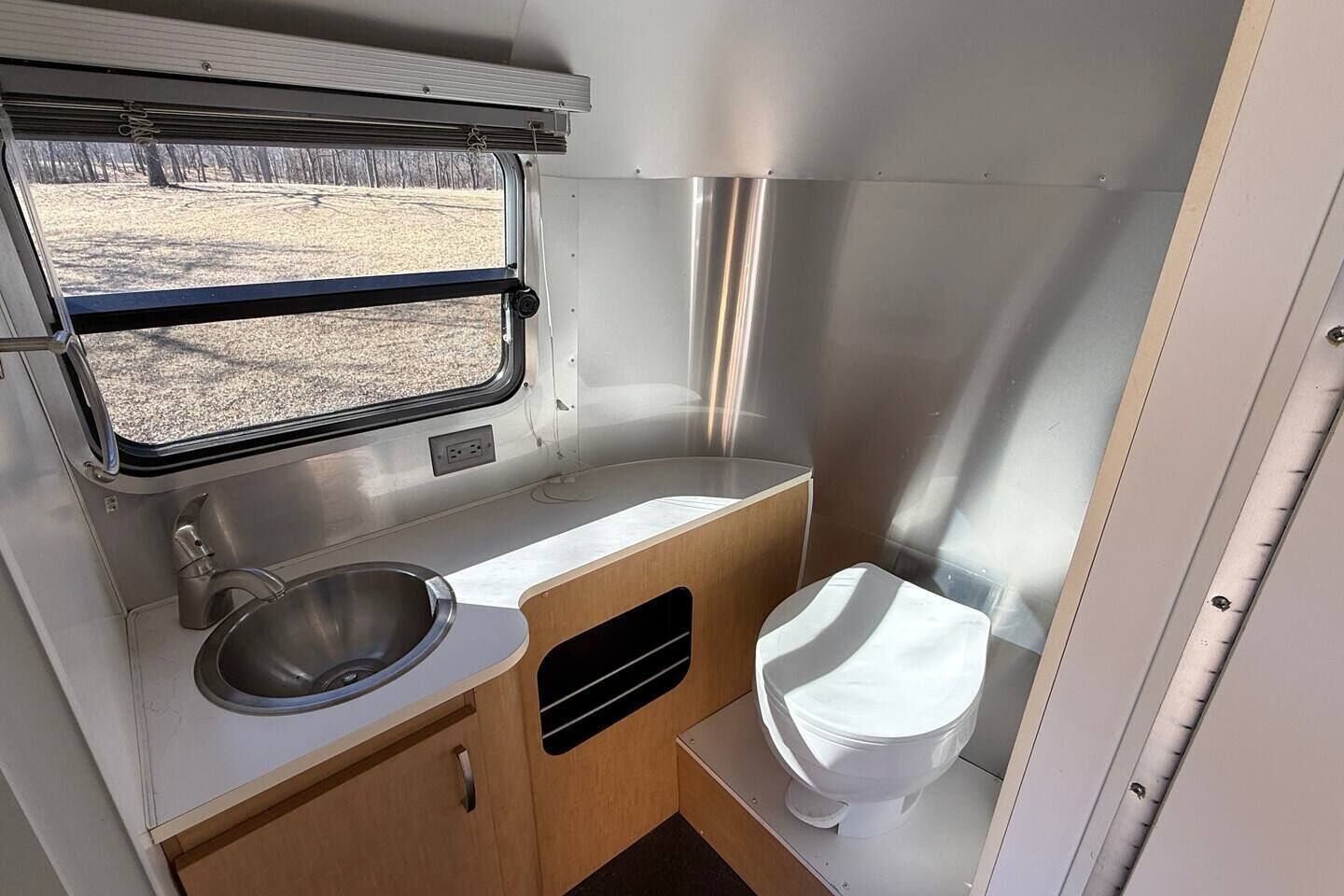 A compact kitchenette with a sink, window, and toilet in a camper.
