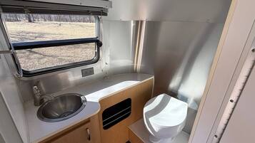 A compact kitchenette with a sink, window, and toilet in a camper.