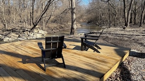 Een houten terras met twee zwarte stoelen en een rivier op de achtergrond.