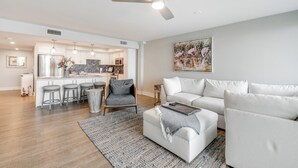 Una sala de estar moderna con un sofá blanco, una mesa de centro y un comedor con taburetes de bar.