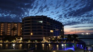 Un hotel de varios pisos con balcones, un área de piscina iluminada y vista al agua.