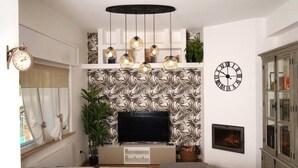 A living room with a flat-screen TV, a grey sofa, a patterned wall, a clock, and a fireplace. - The Rose Cottage (Tavernelle)