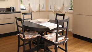 A dining area with a round table, four chairs, a hanging light fixture, and a window with curtains. - The Rose Cottage (Tavernelle)