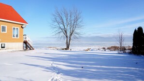 A snow-covered landscape with a house featuring a red roof and a visible staircase leading to a deck.