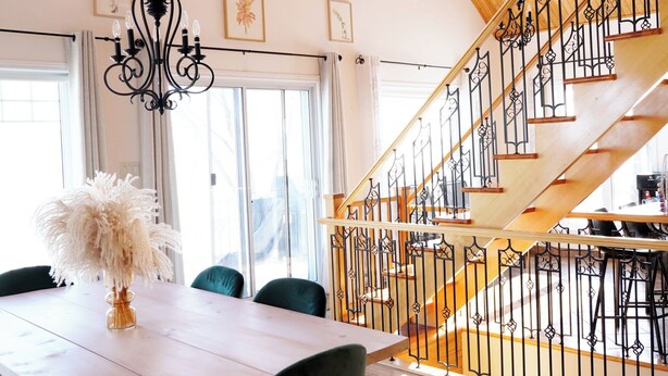 A spacious dining area with a high ceiling, wooden beams, and a staircase with a wrought iron railing.